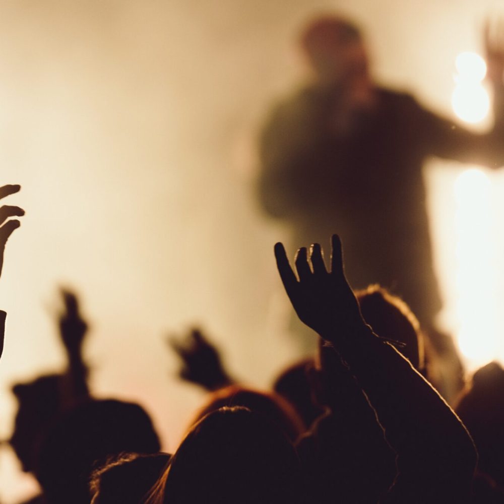 People dancing at a concert while the singer is performing surrounded with lights